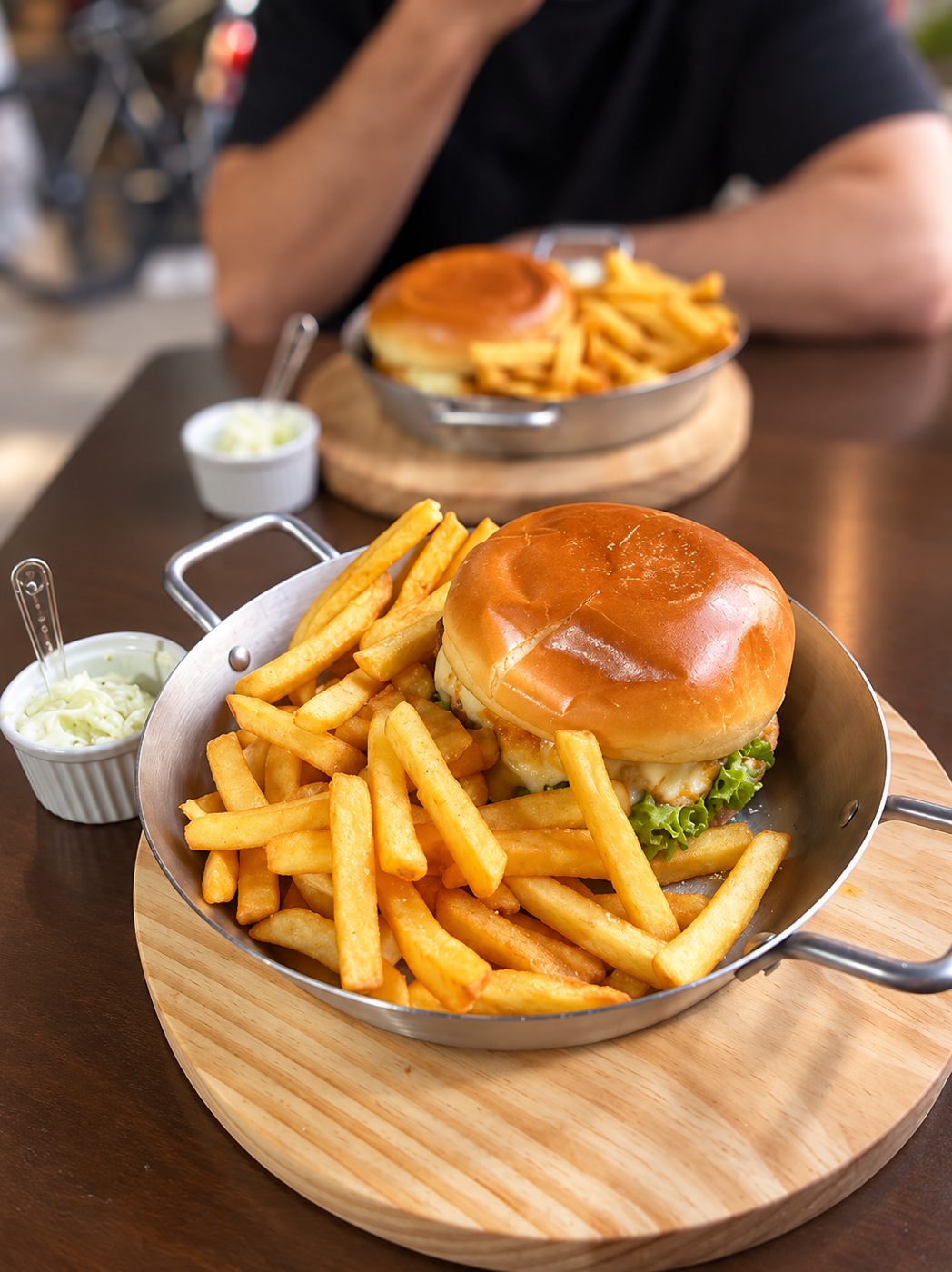 Hambúrguer com fritas servido em panelinha de inox sobre tábua de madeira